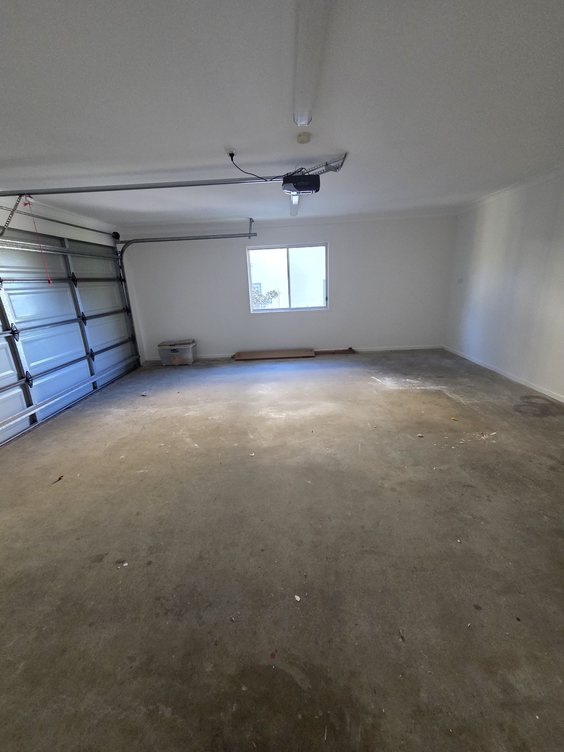 Empty garage with concrete floor, white walls, a window, and a closed garage door.