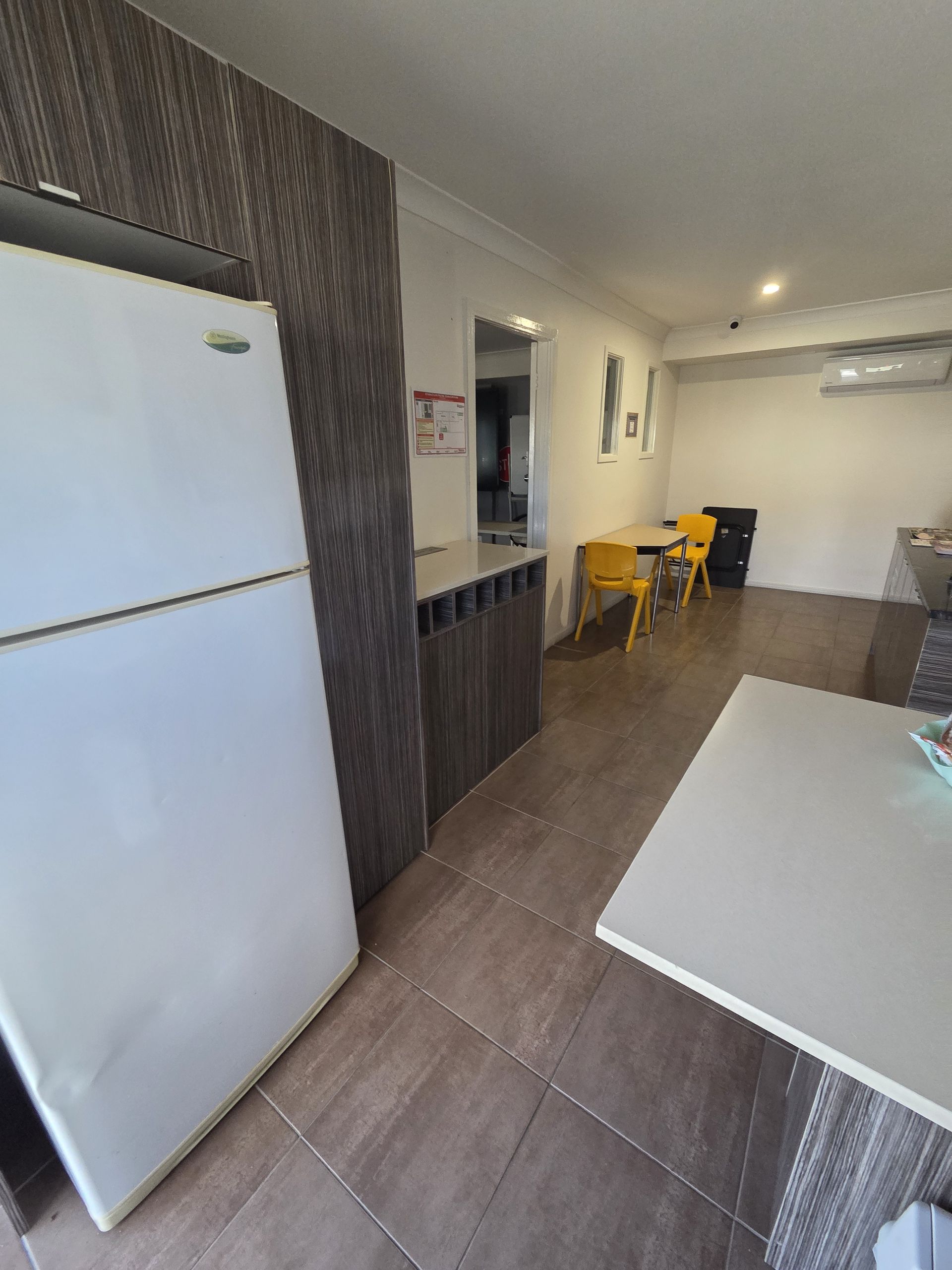 Small kitchen with white refrigerator, counters, and a dining table leading into a living area.