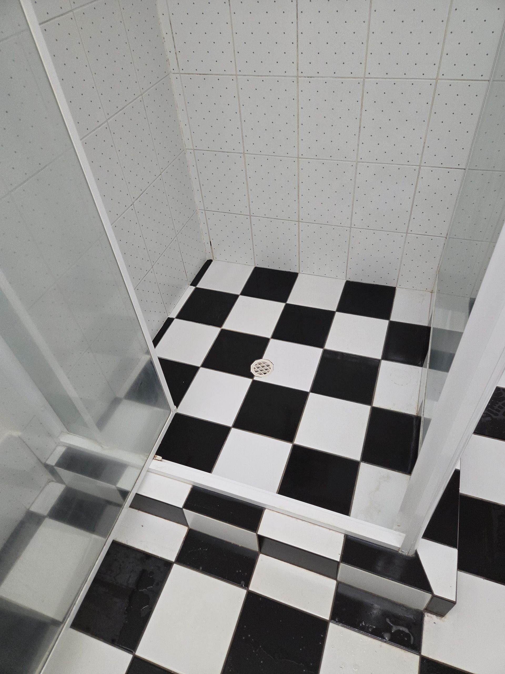 Small tiled shower stall with black-and-white checkered floor and white wall tiles.