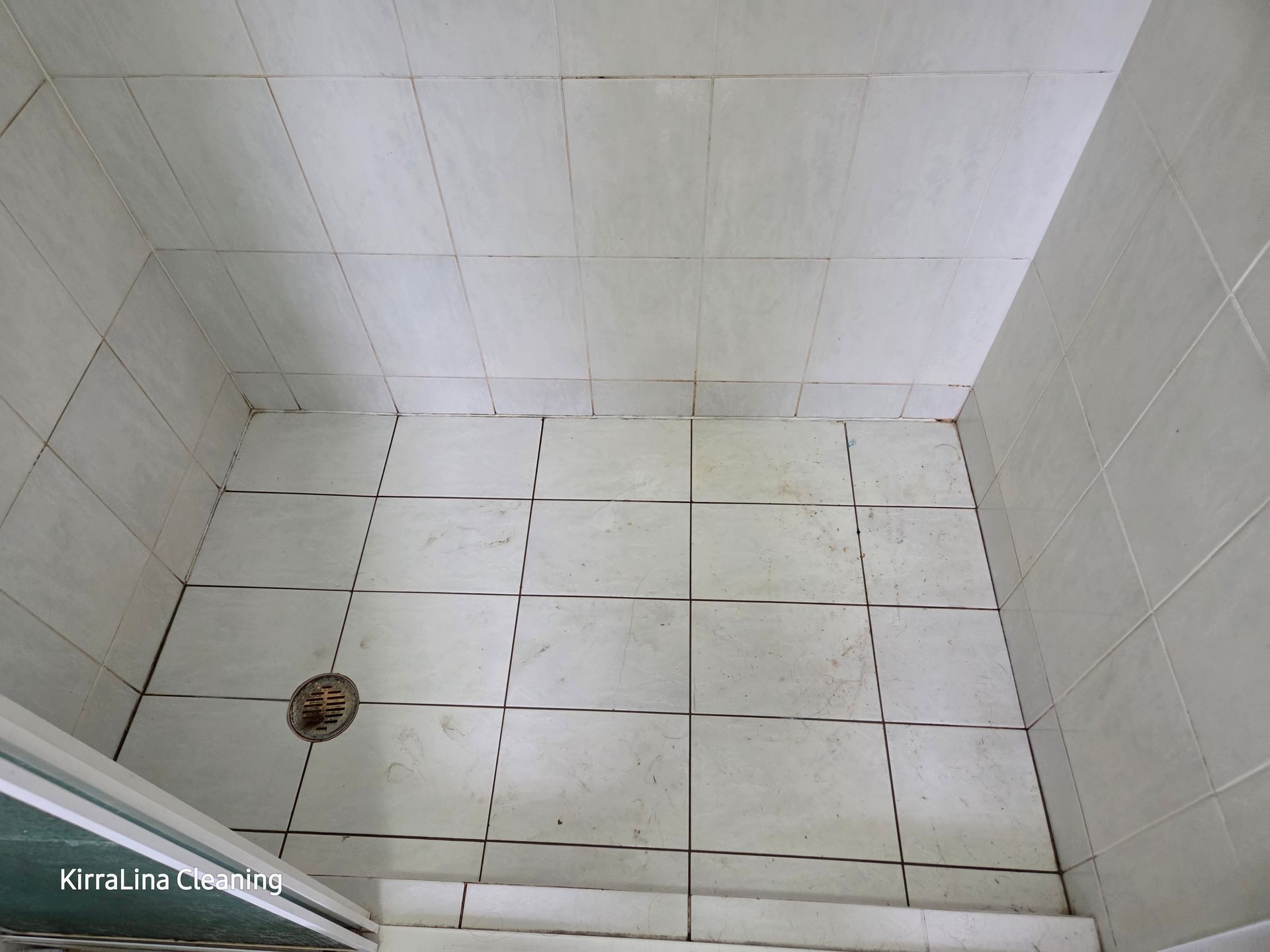 White Tiled Shower Corner With a Floor Drain and Dark Grout Stains — KirraLina Cleaning Services in Tweed Heads, NSW