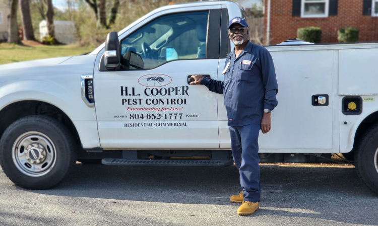 Man in blue uniform stands by a white pest control truck with 