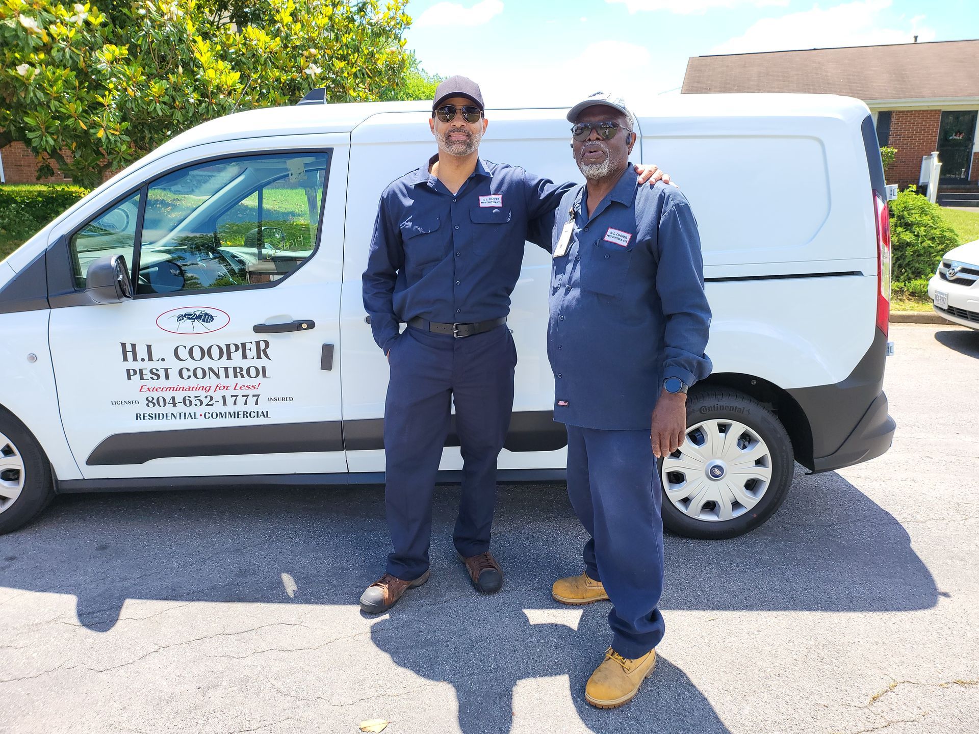 Two men in matching uniforms stand beside a white van with business logo in a parking lot.