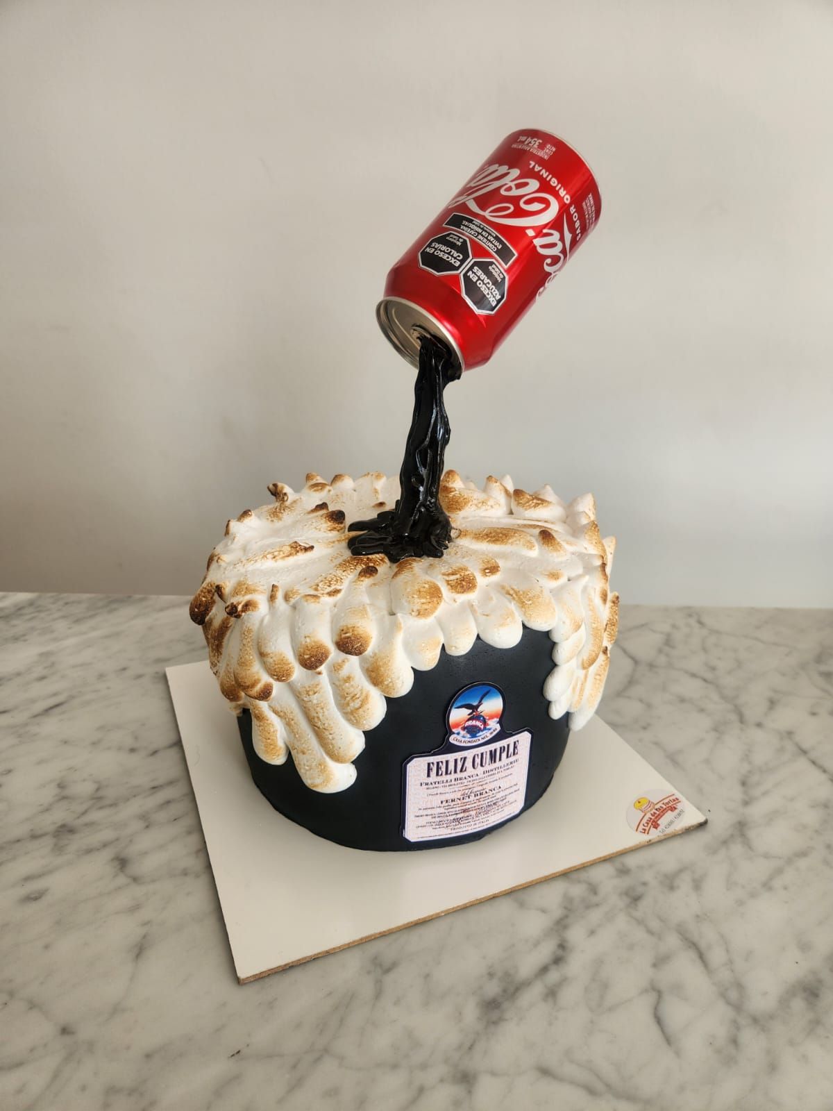 Pastel de chocolate cubierto con una lata de refresco roja goteando y crema blanca sobre una encimera de mármol.