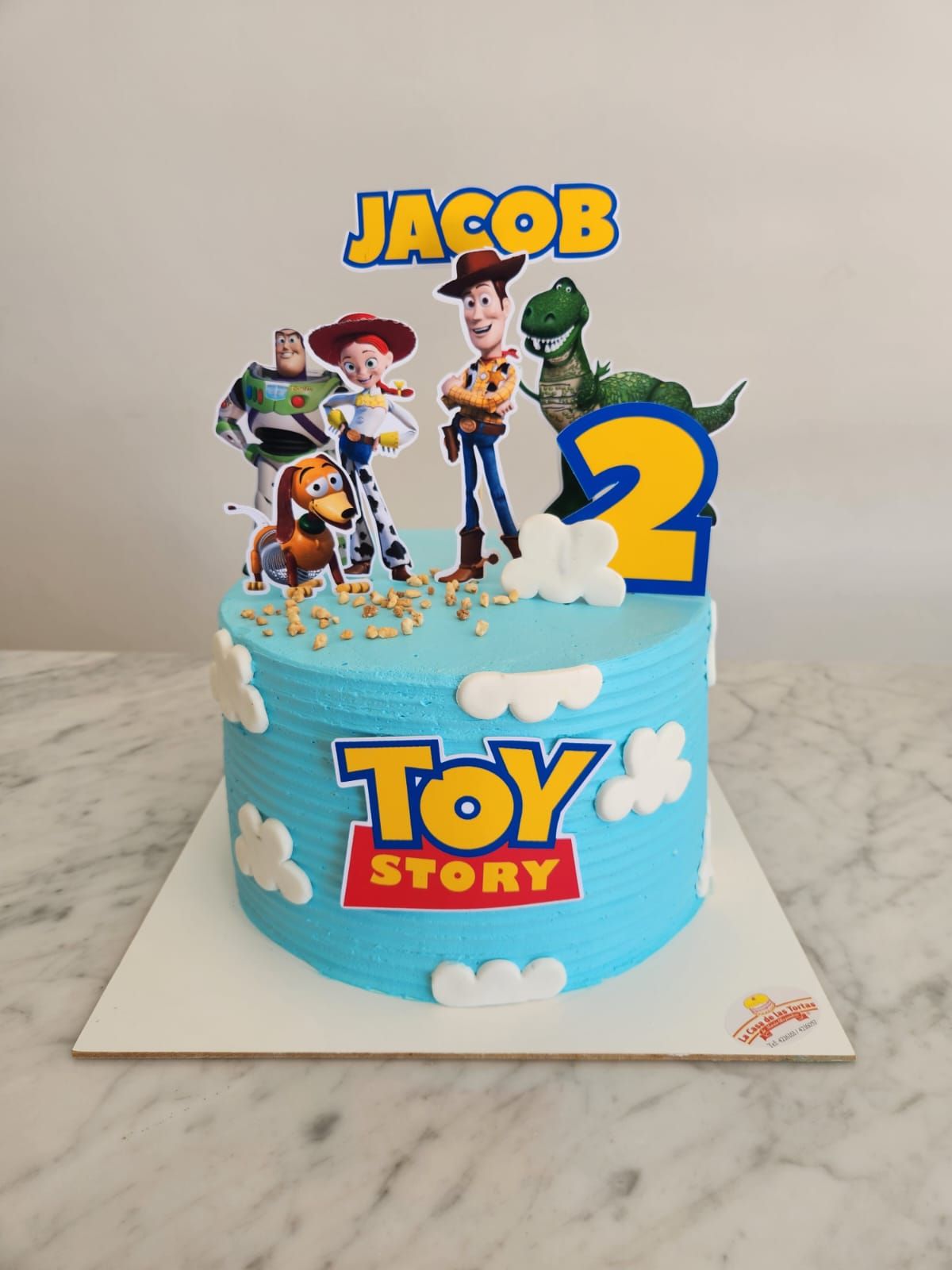 Tarta de cumpleaños de Toy Story con adornos de Woody, Buzz, Jessie, Rex, Jacob y el número 2 azul.