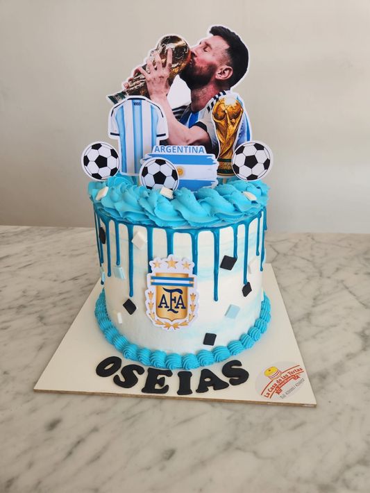 Tarta de cumpleaños azul con temática futbolística, decorada con una figurita, balones de fútbol.