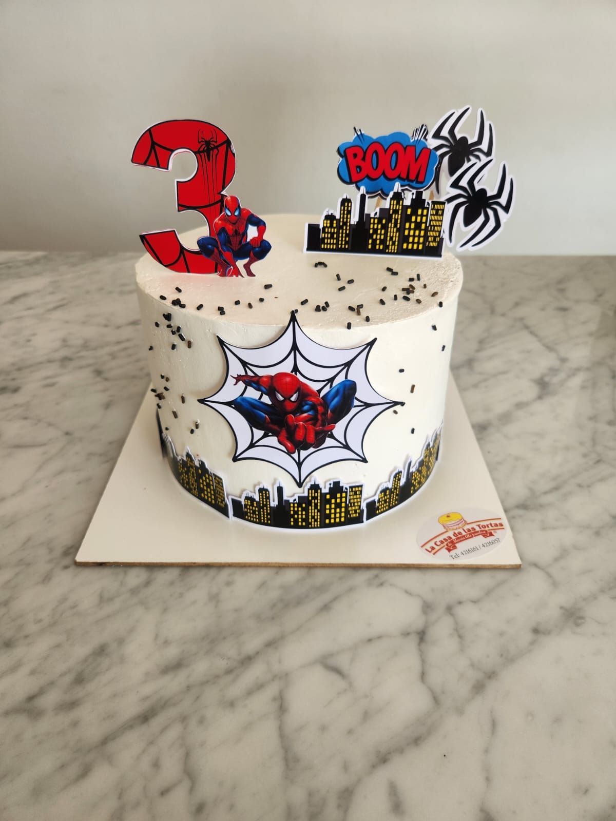 Tarta blanca con adornos de Spider-Man y estilo cómic sobre una encimera de mármol.