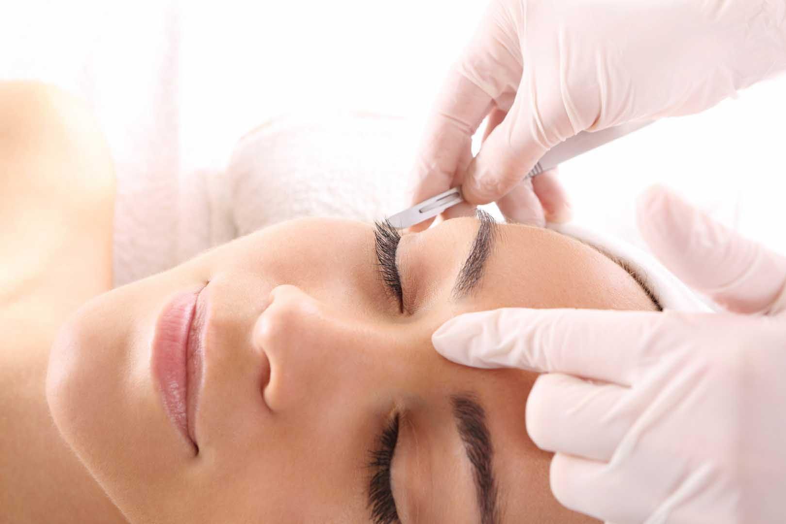 Person receiving eyebrow threading; gloved hands holding thread near face.