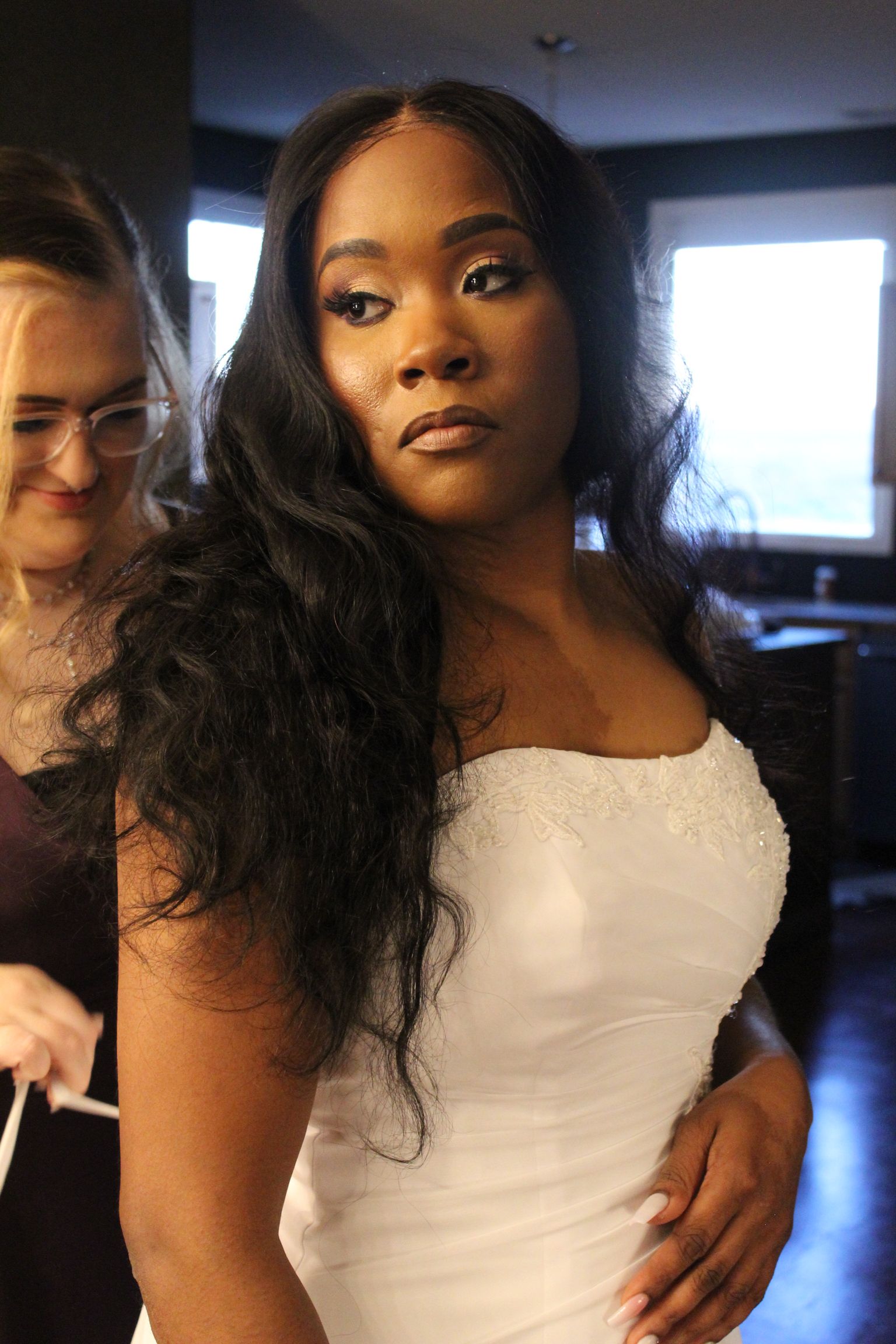 bride with dress being tied, looking in mirror over shoulder