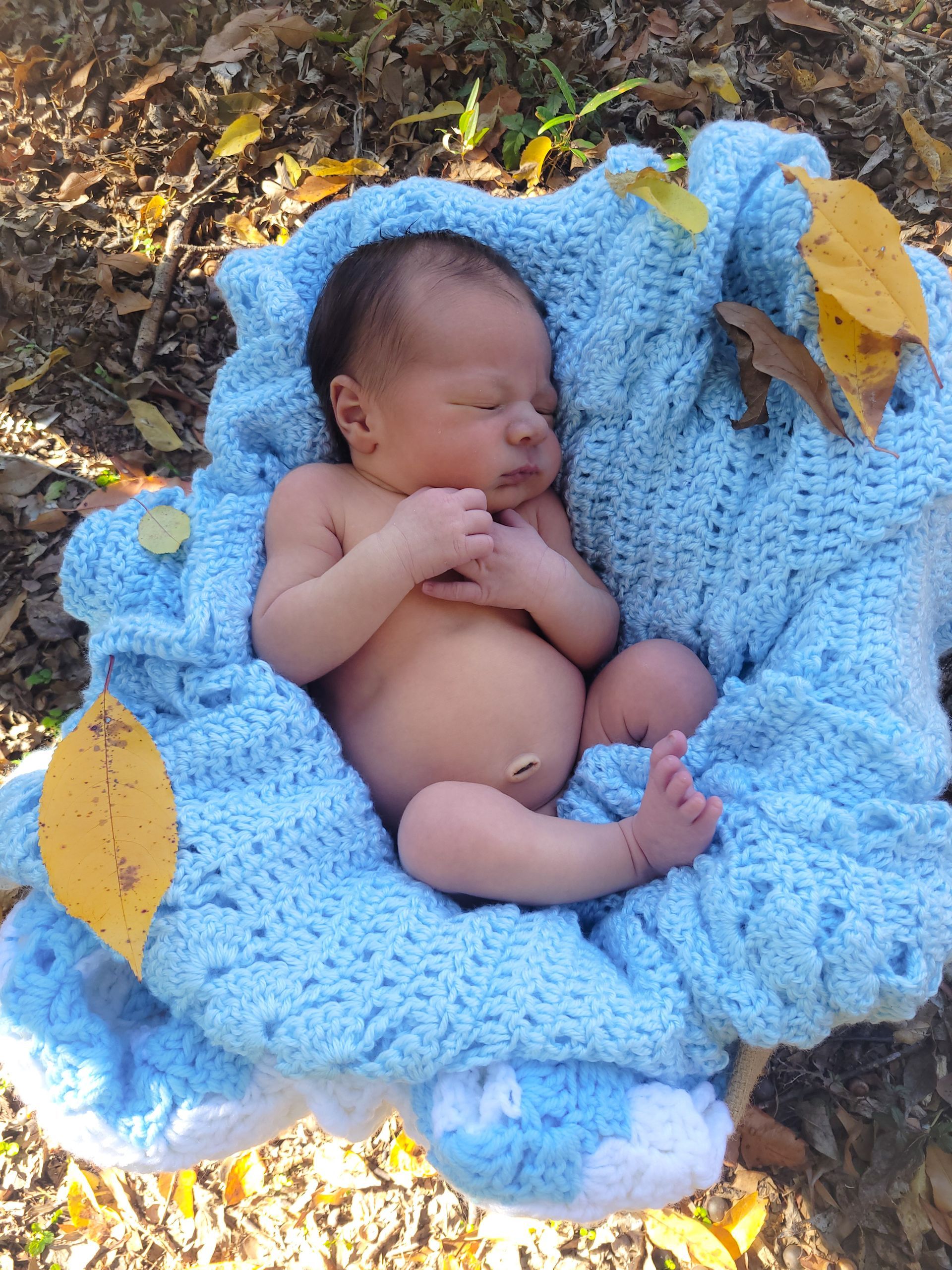 newborn sleeping in crochet blanket with fall leaves