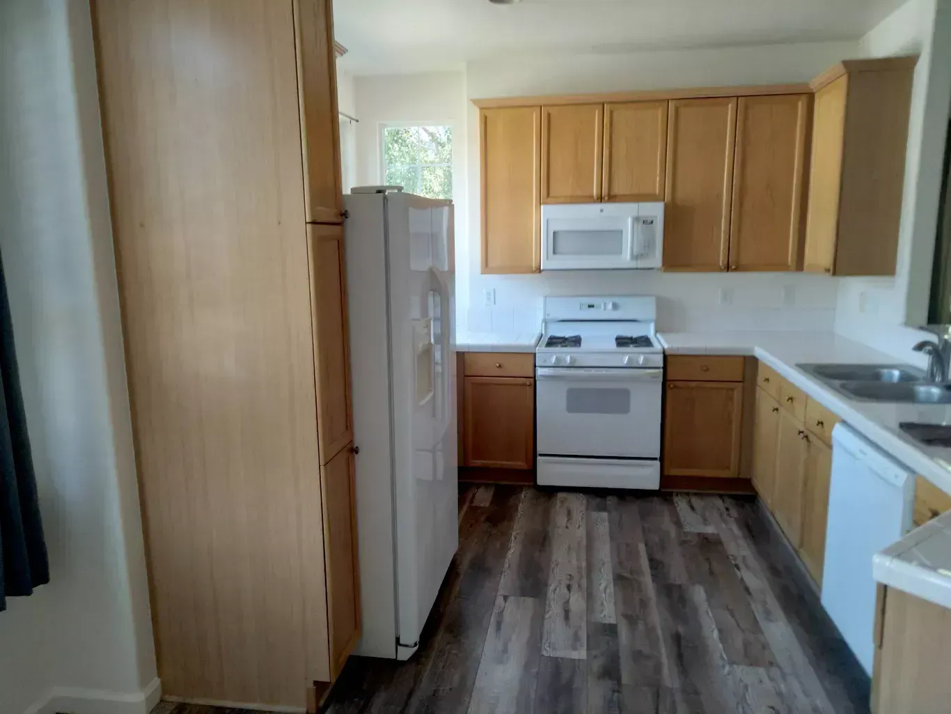 Small kitchen with light wood cabinets, white appliances, and a wood-look floor.