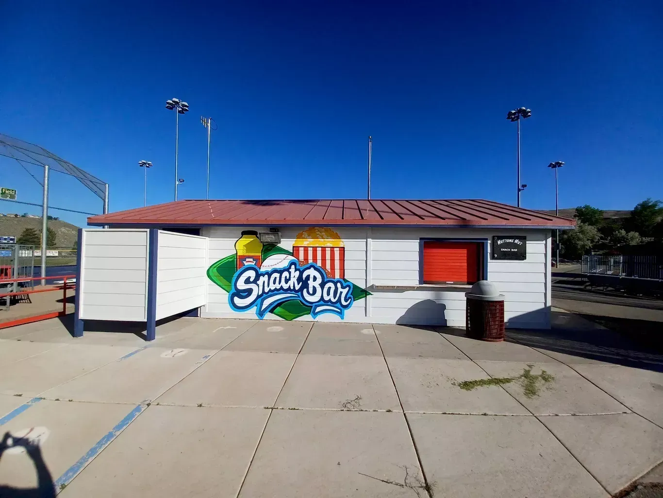Small snack bar building with a colorful mural and red roof on a sunny day
