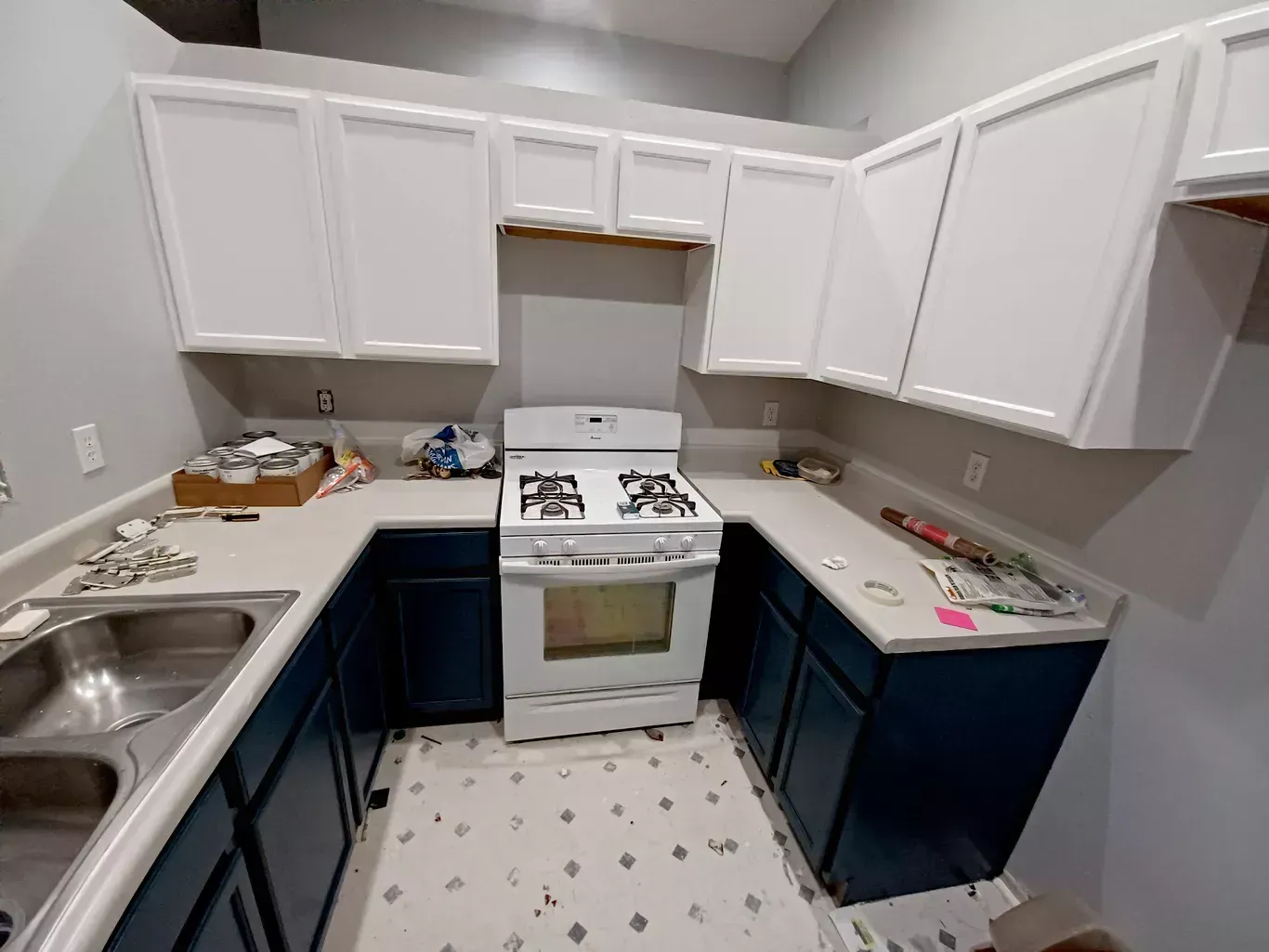 Small U-shaped kitchen with white upper cabinets, dark lower cabinets, a gas stove, and a sink on the left.