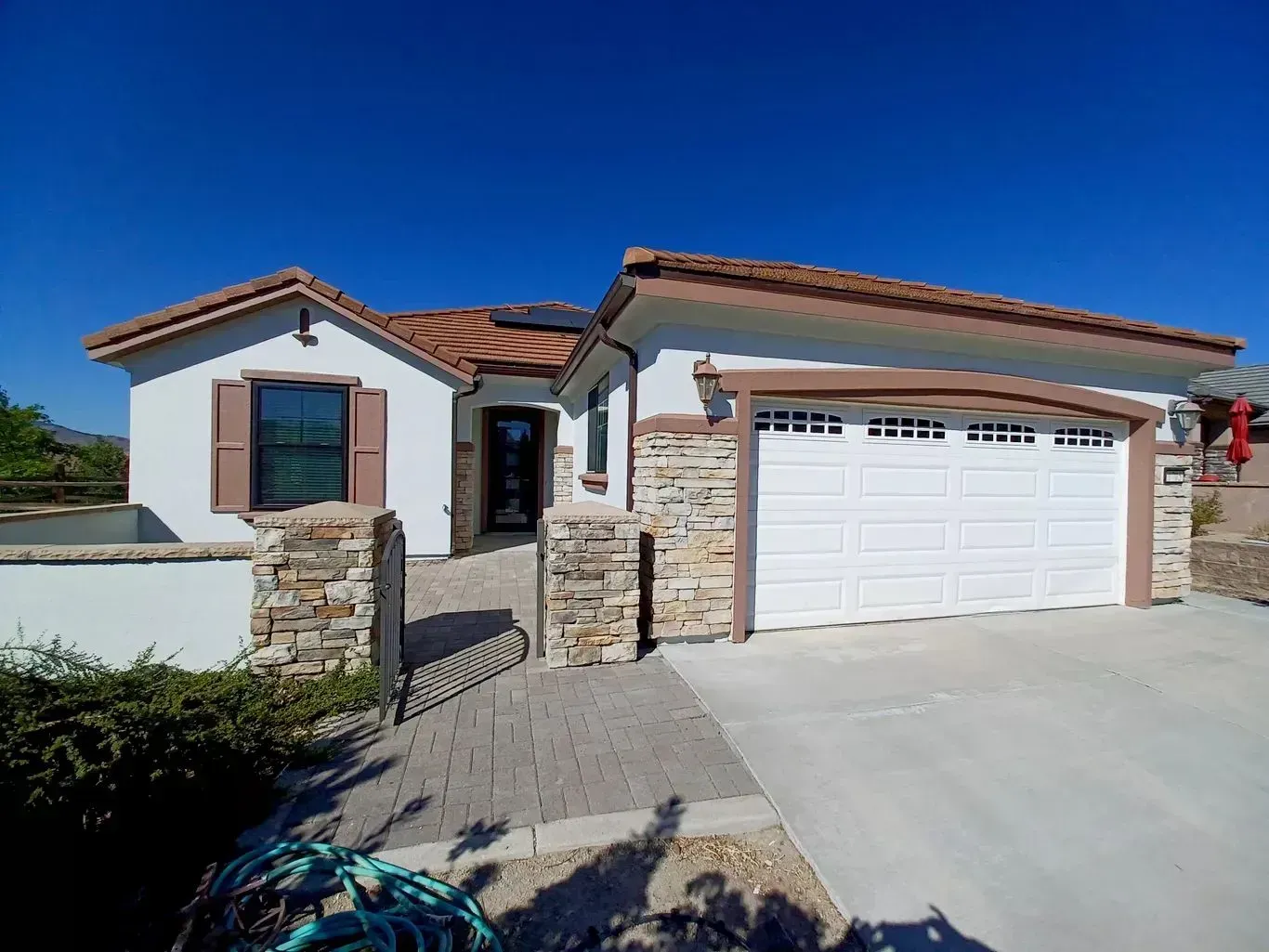Single-story stucco house with red tile roof, stone entry, and white garage door under a blue sky