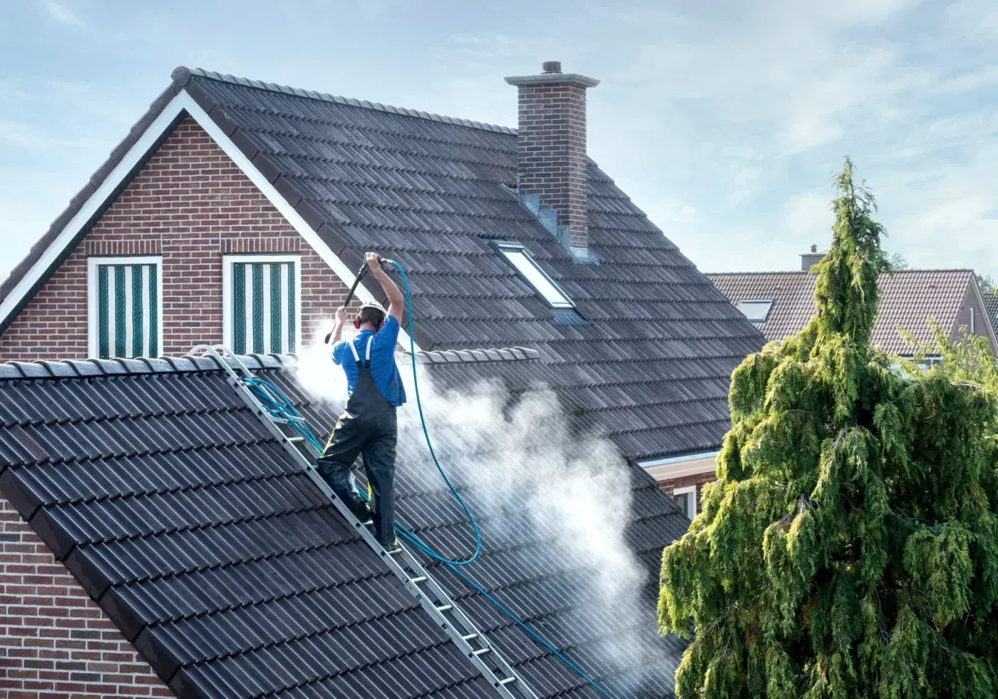 A man is cleaning the roof of a house with a pressure washer.