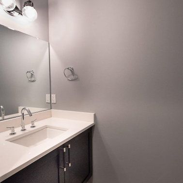Bathroom with a white countertop, dark cabinets, a mirror, and gray walls.