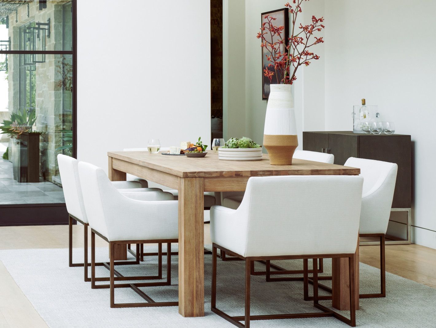 Dining room with light wood table, white chairs, and decorative vase.
