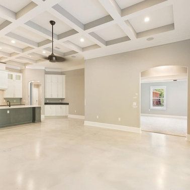 Empty, modern, neutral-toned room with coffered ceiling, fan, and large doorway leading to another room.