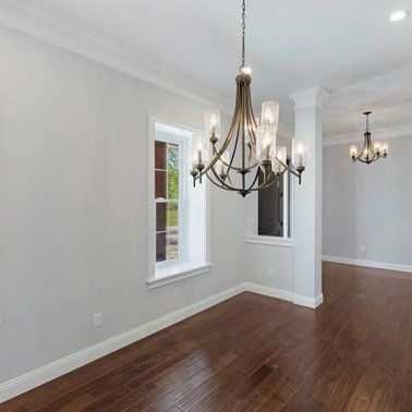 Empty dining room with dark wood floors, light gray walls, white trim, and two chandeliers.