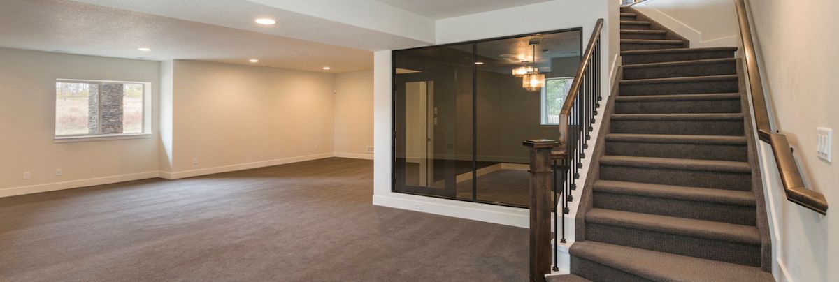 An open interior with stairs, a large window, and empty rooms with neutral walls and carpet.