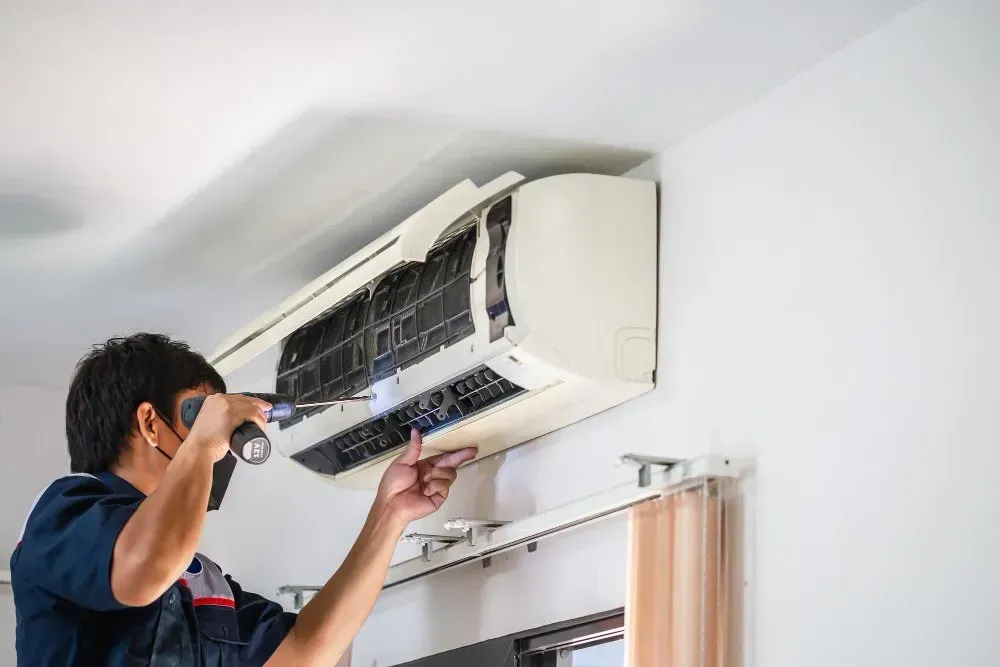 Technician inspecting a white air conditioning unit with a flashlight, indoors.