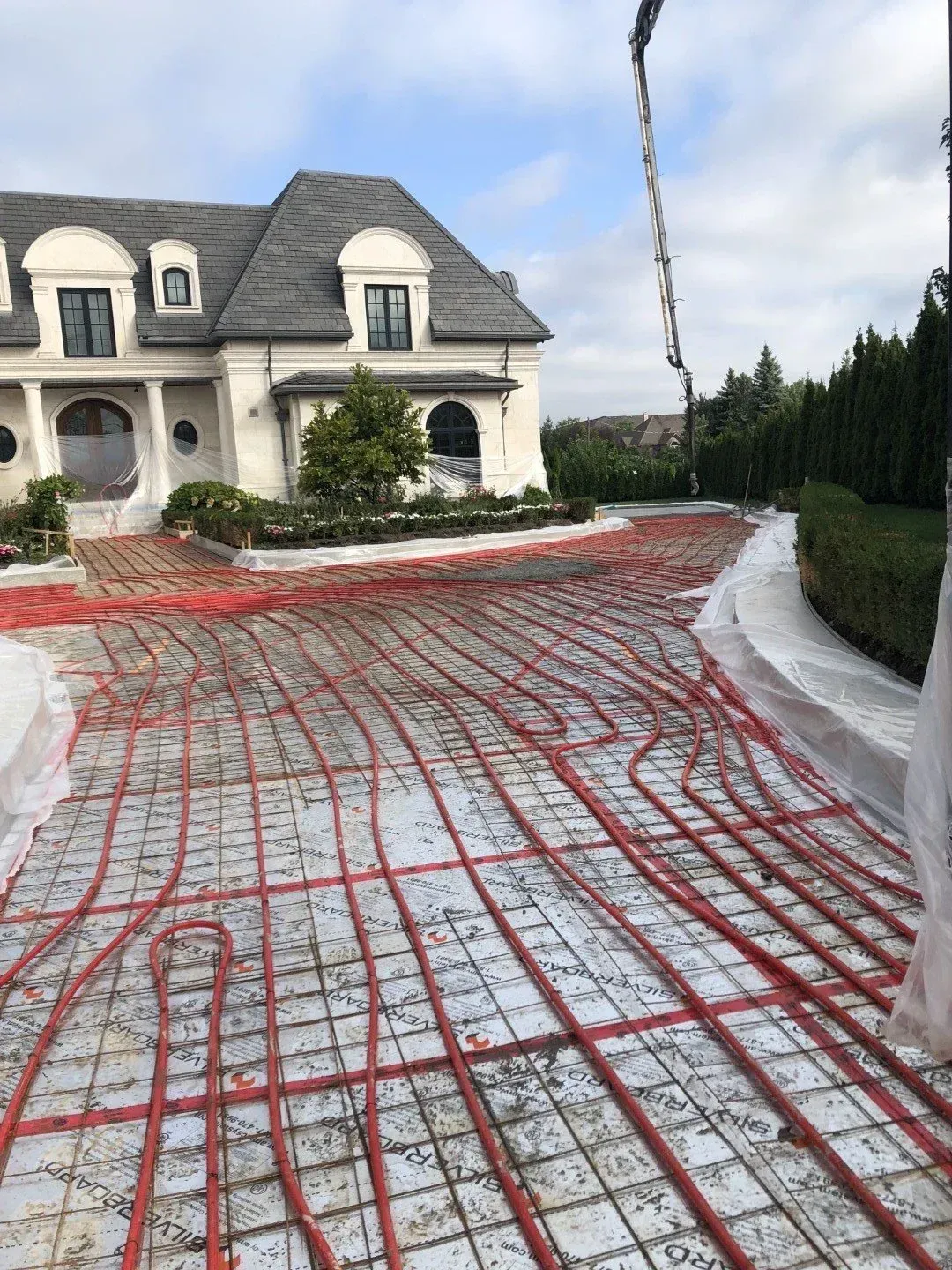 Driveway construction: red radiant heating tubes laid on wire mesh in front of a large house with a gray roof.