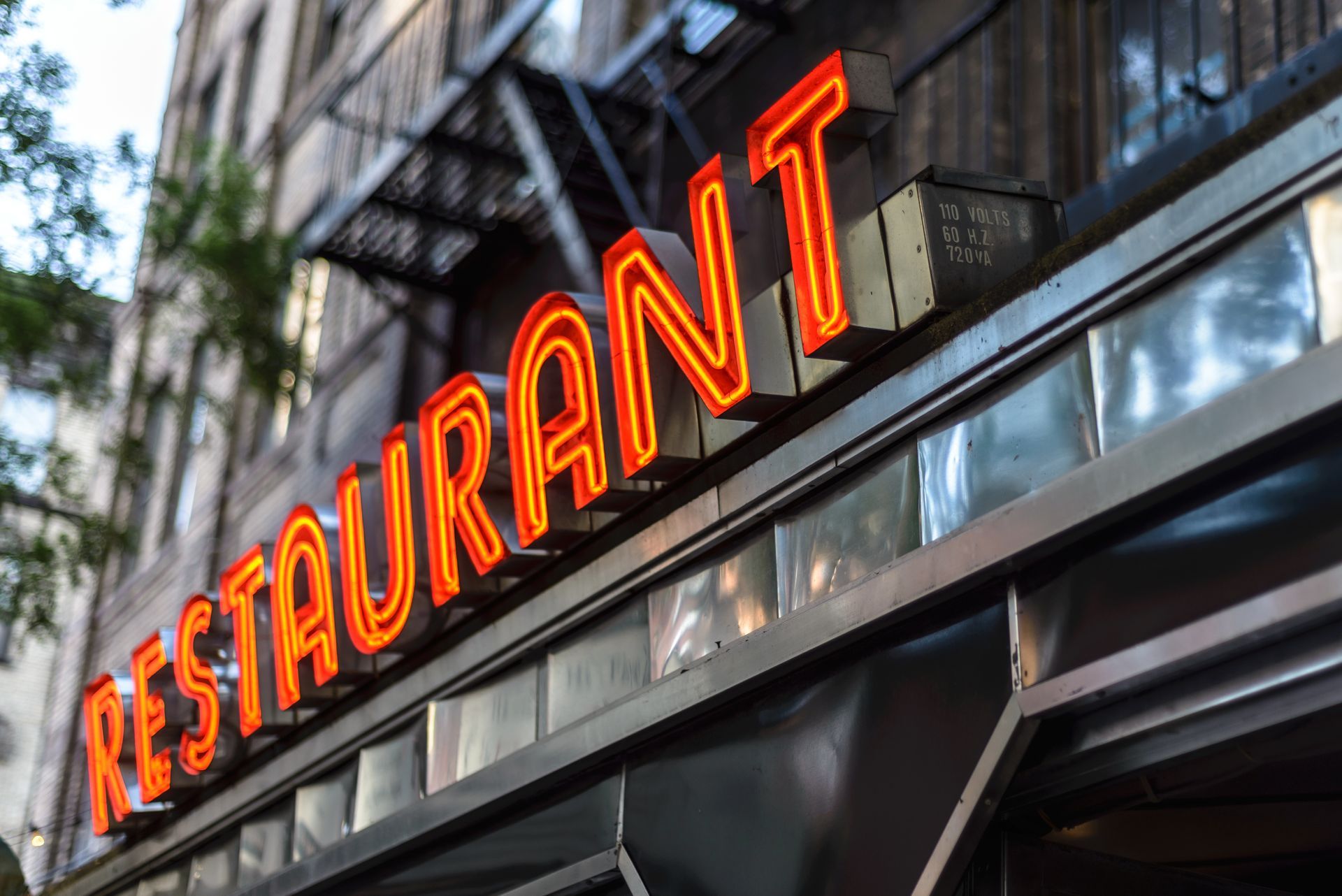 Neon “RESTAURANT” sign above a city storefront with blurred urban background. Neon “RESTAURANT” sign above a city storefront with blurred urban background.