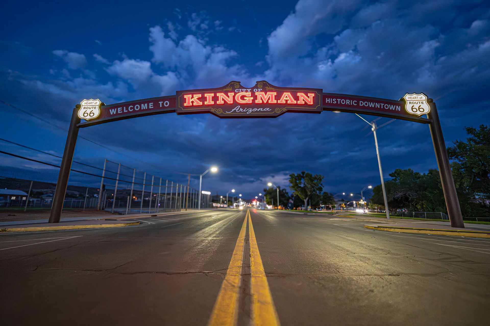 Kingman, Arizona welcome archway at dusk with illuminated sign over an empty road.