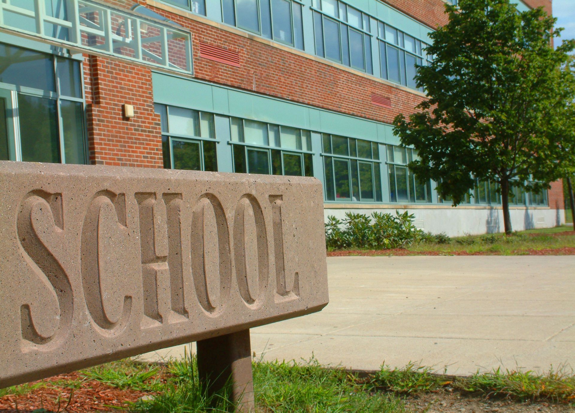 A large engraved stone school signage in Chandler, AZ, stands in front of a modern school building, designed by Precise Sign.