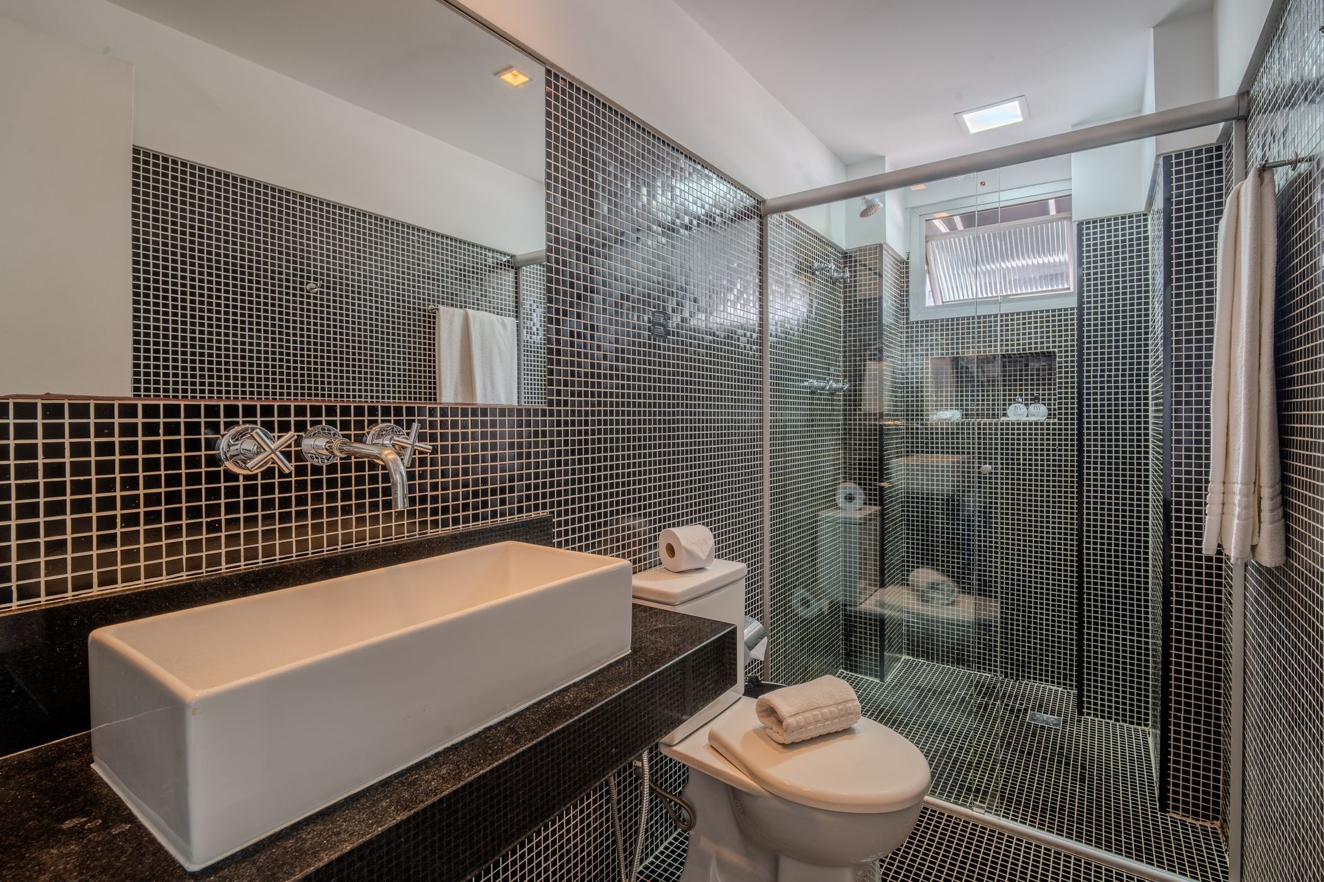 Um banheiro moderno com uma pia de apoio branca, um vaso sanitário e paredes revestidas com azulejos em um padrão geométrico ondulado e quadriculado em preto e branco.