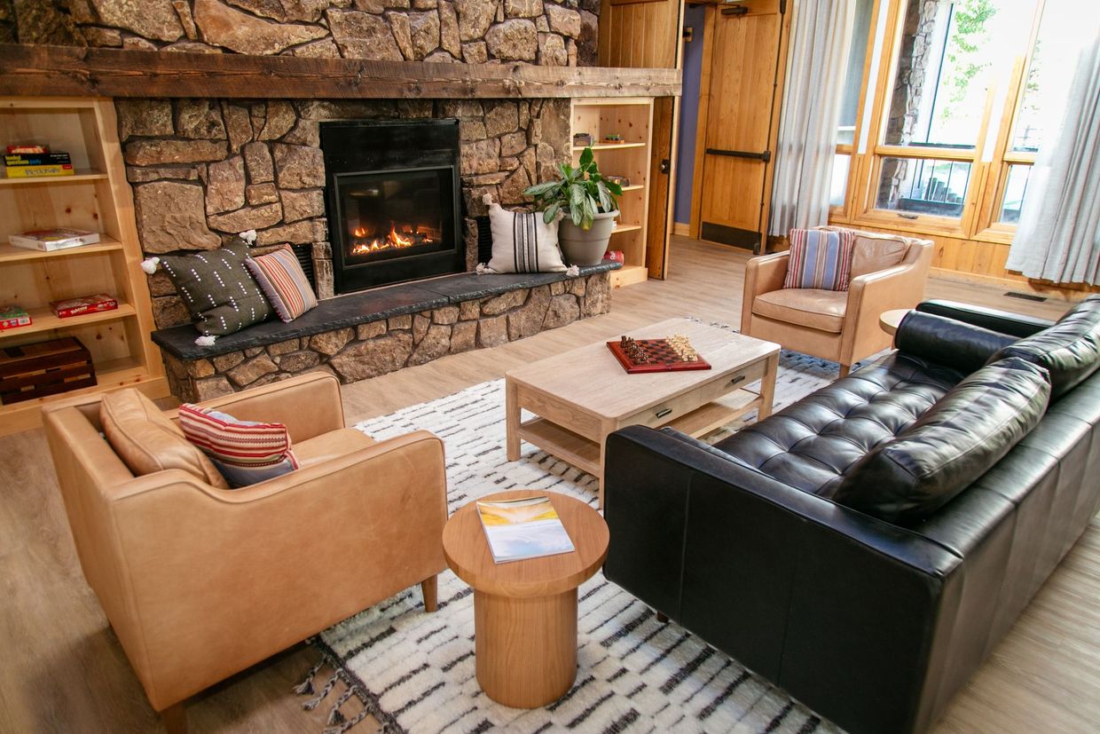 Cozy living room with stone fireplace, tan armchairs, black sofa, and coffee table by large windows