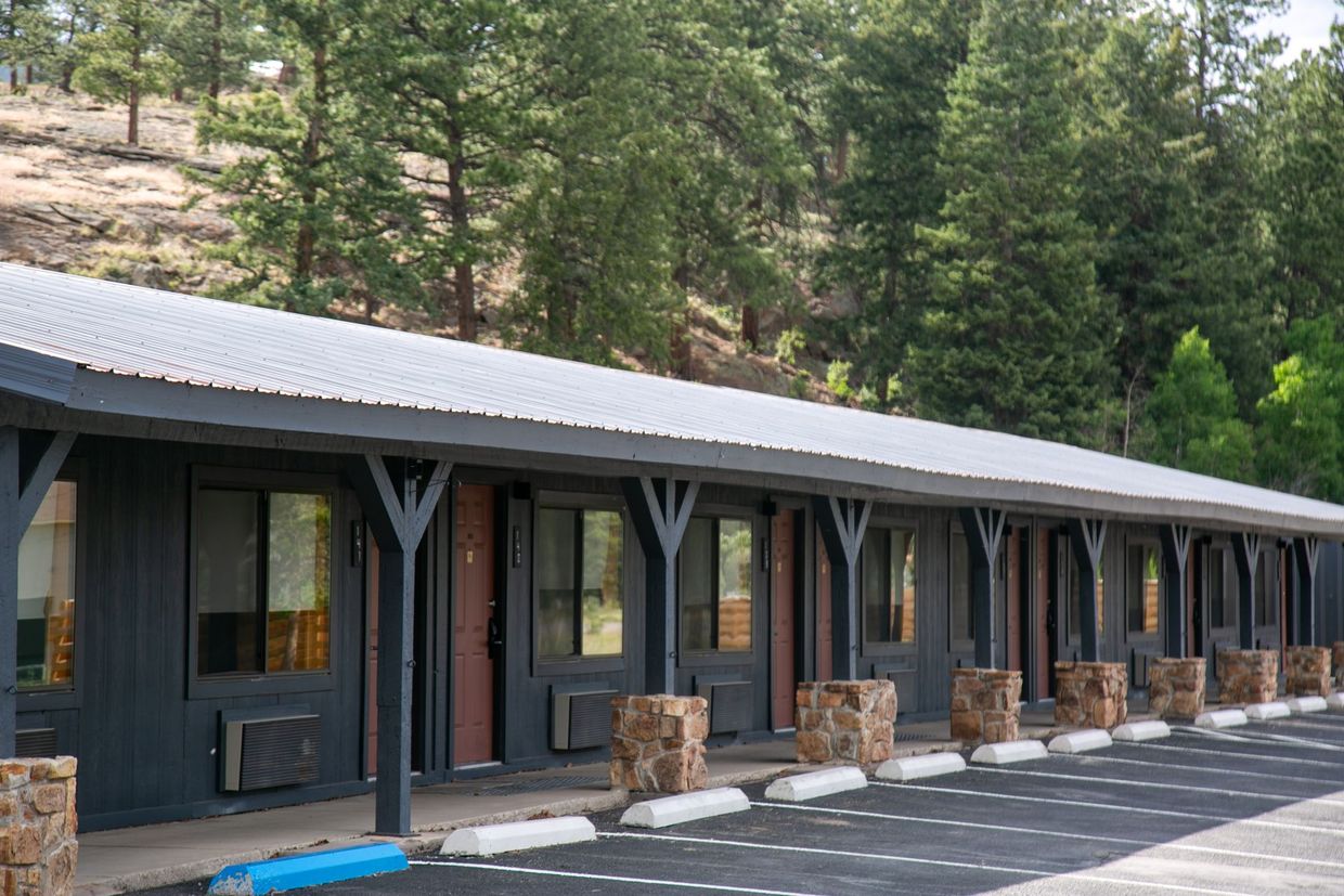 Row of dark cabins with covered porch and parking spots beside a wooded hillside