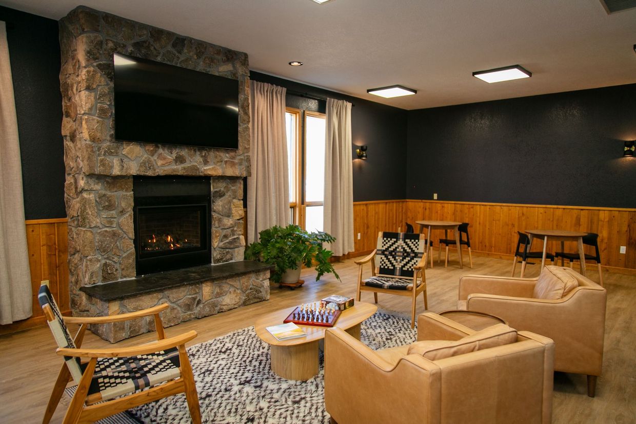 Modern lounge with stone fireplace, tan sofas, wooden chairs, and a wall-mounted TV