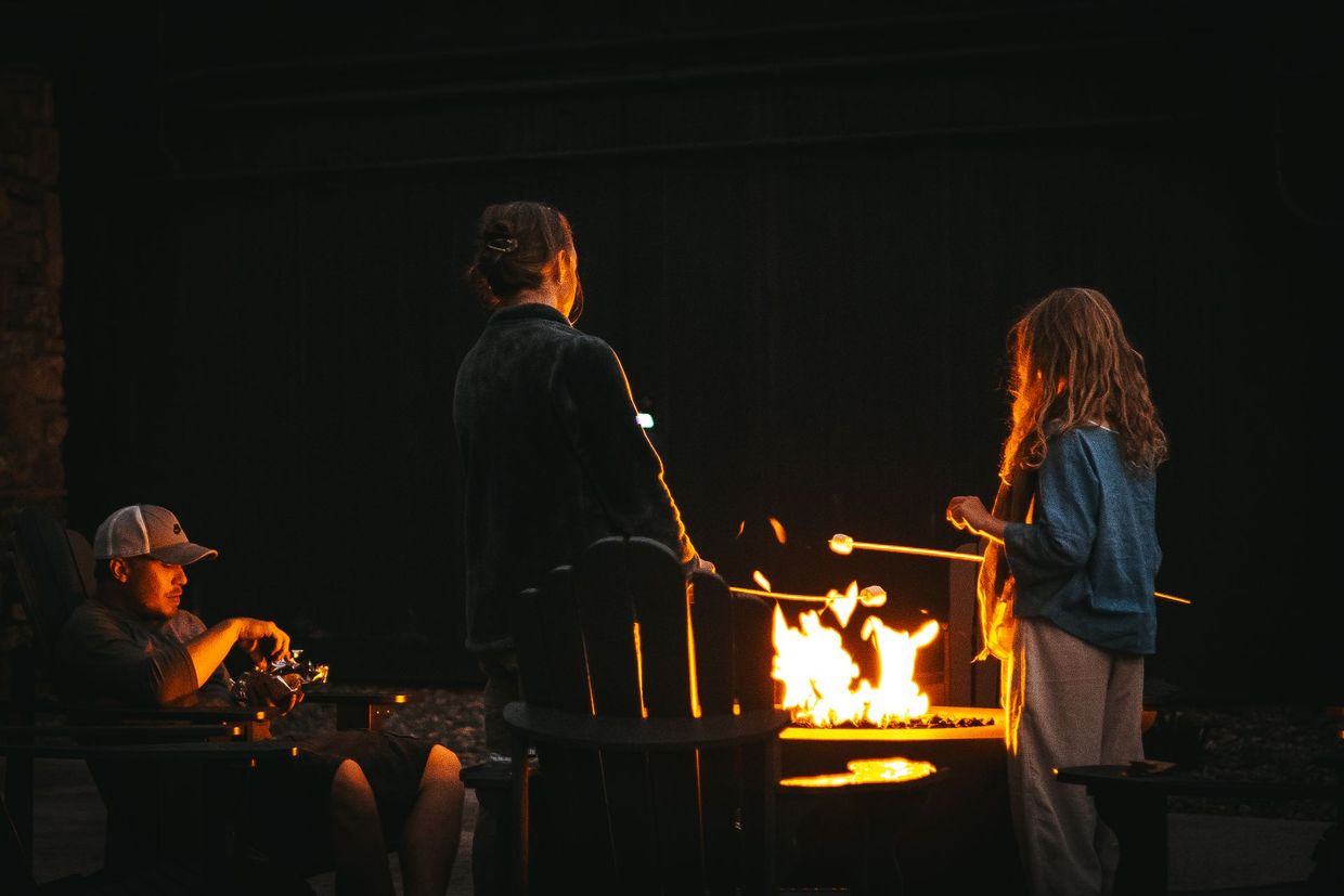 Three people gathered around a glowing fire outdoors at night