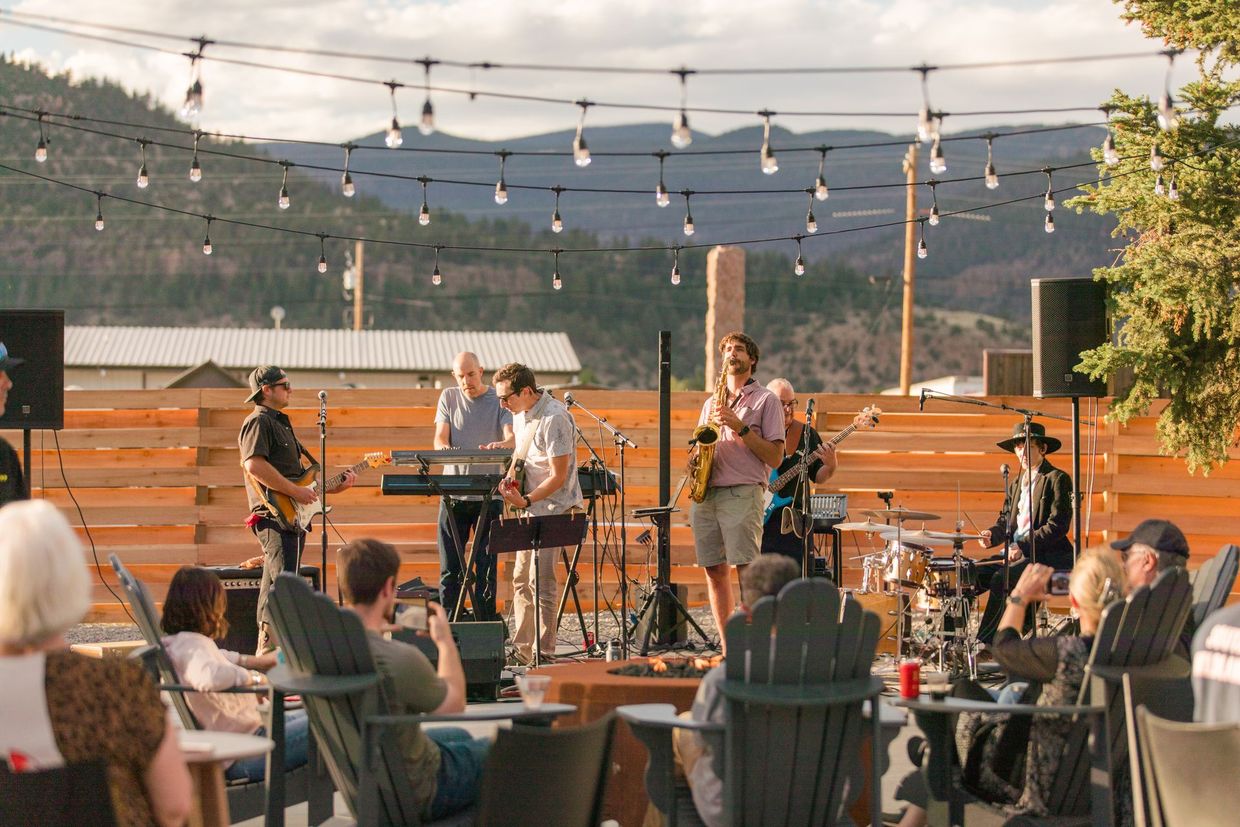 Outdoor live band performing on a patio at sunset, with seated audience and string lights overhead