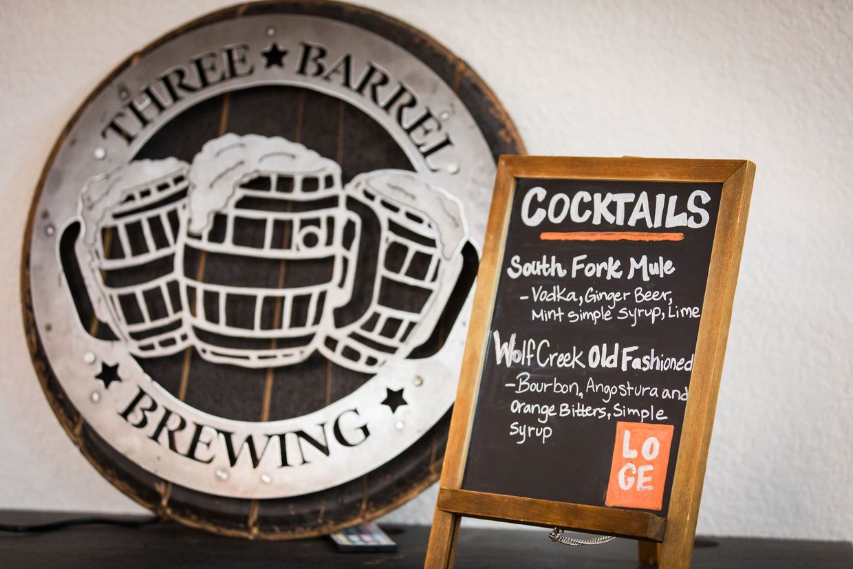 Beer barrel brewing sign beside a chalkboard cocktail menu on a small easel.