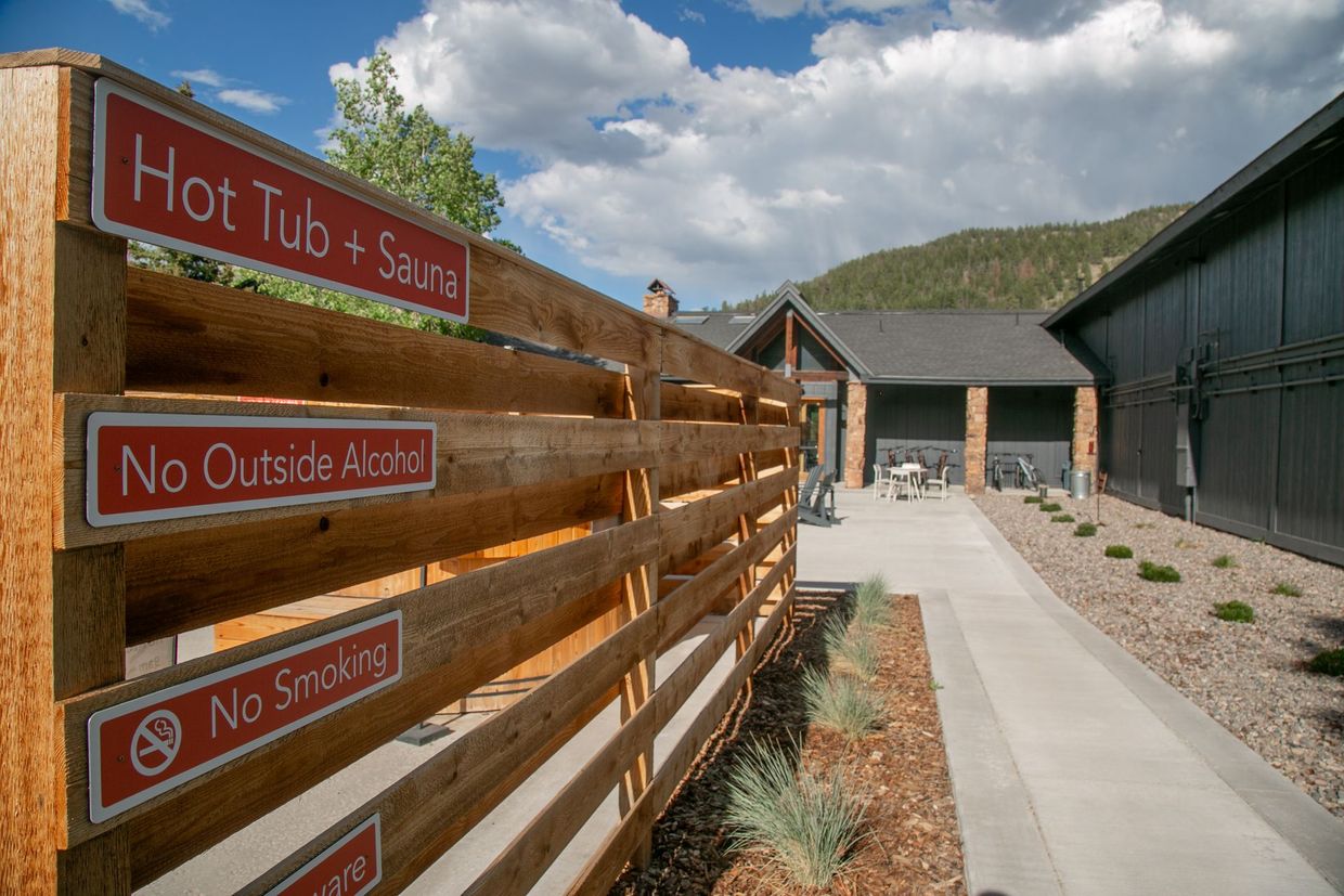 Wooden fence with red warning signs beside a paved walkway and cabins under a cloudy sky