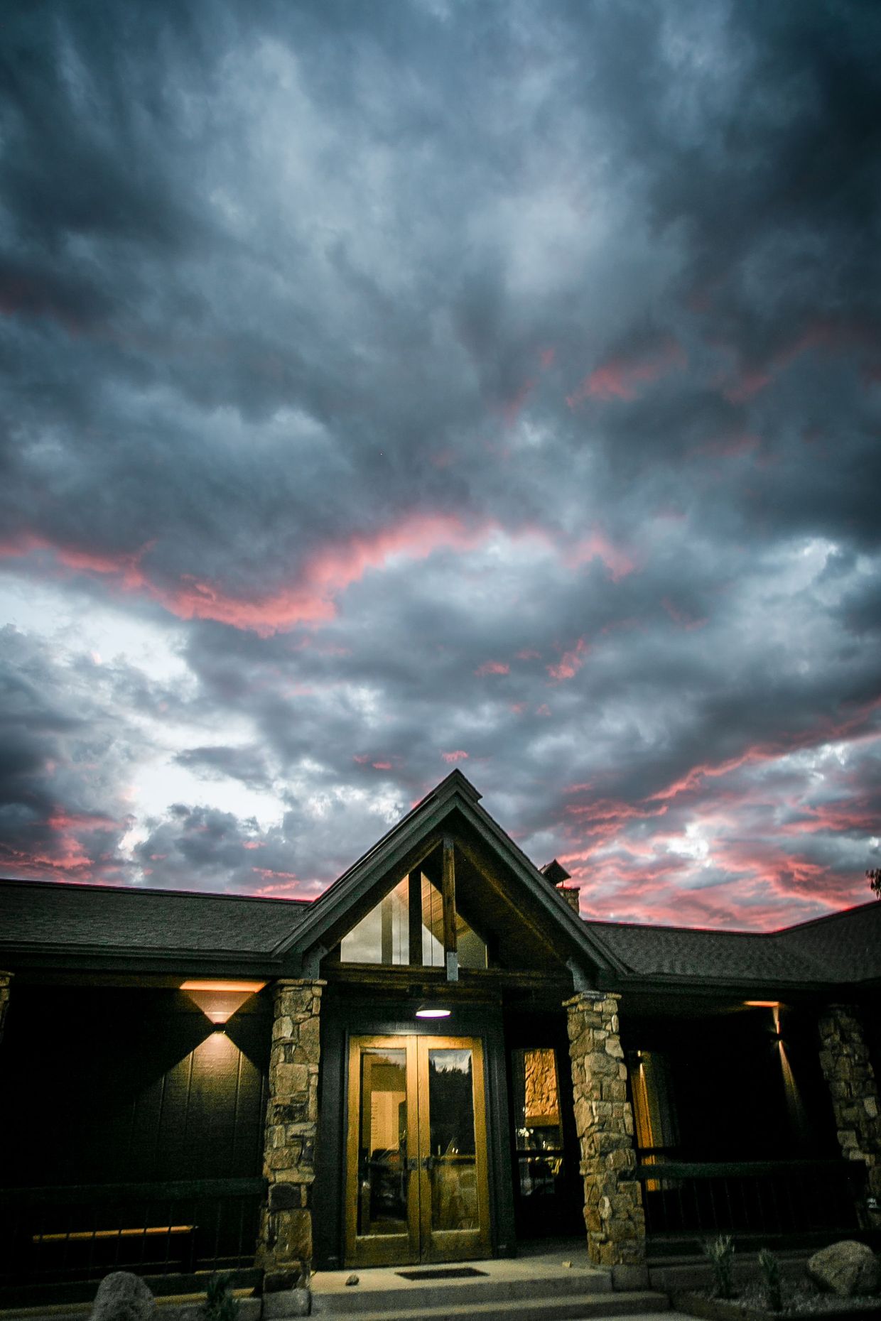 Lit house entrance under dramatic pink-streaked storm clouds at dusk