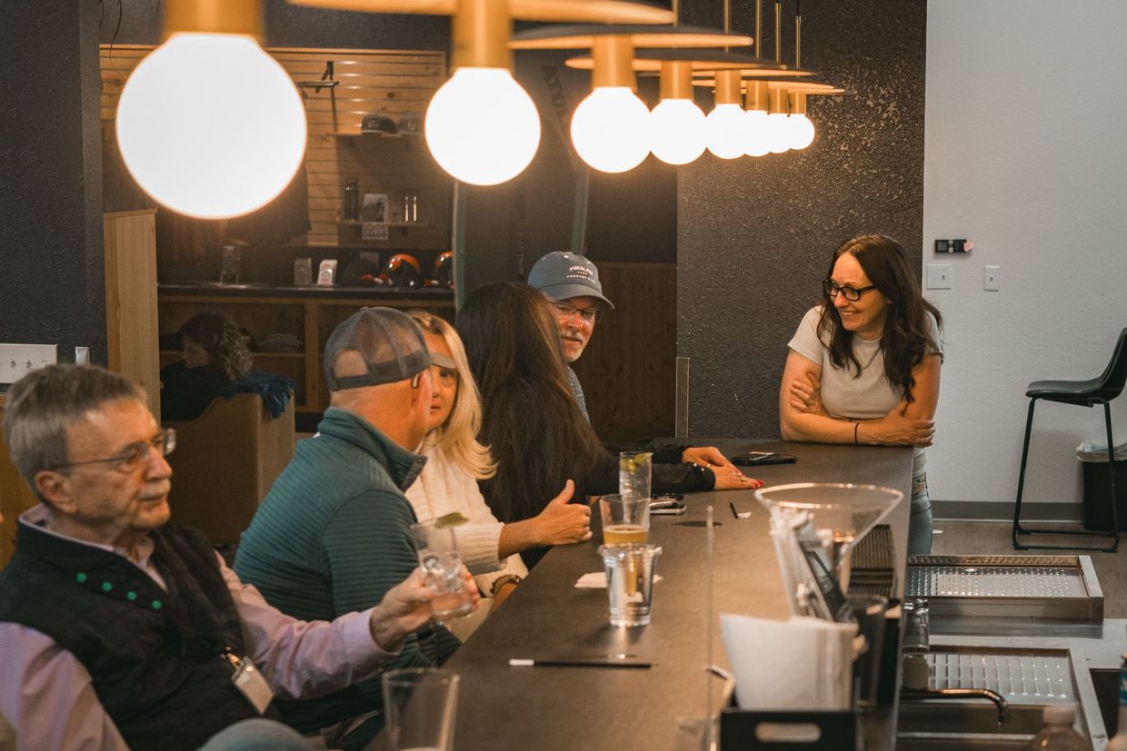 People seated at a café counter under hanging lights, chatting over drinks