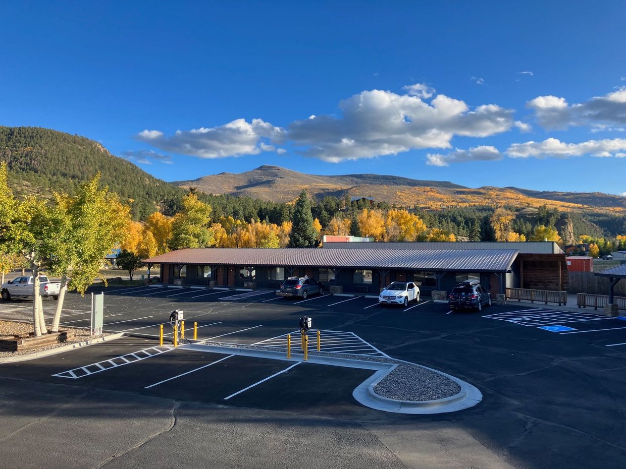 Mountain lodge parking lot with parked cars, yellow trees, and mountains under a blue sky