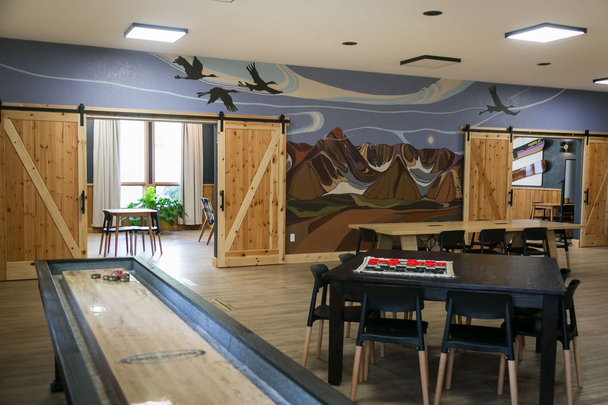 Indoor game room with shuffleboard, pool table, and mountain mural on the wall