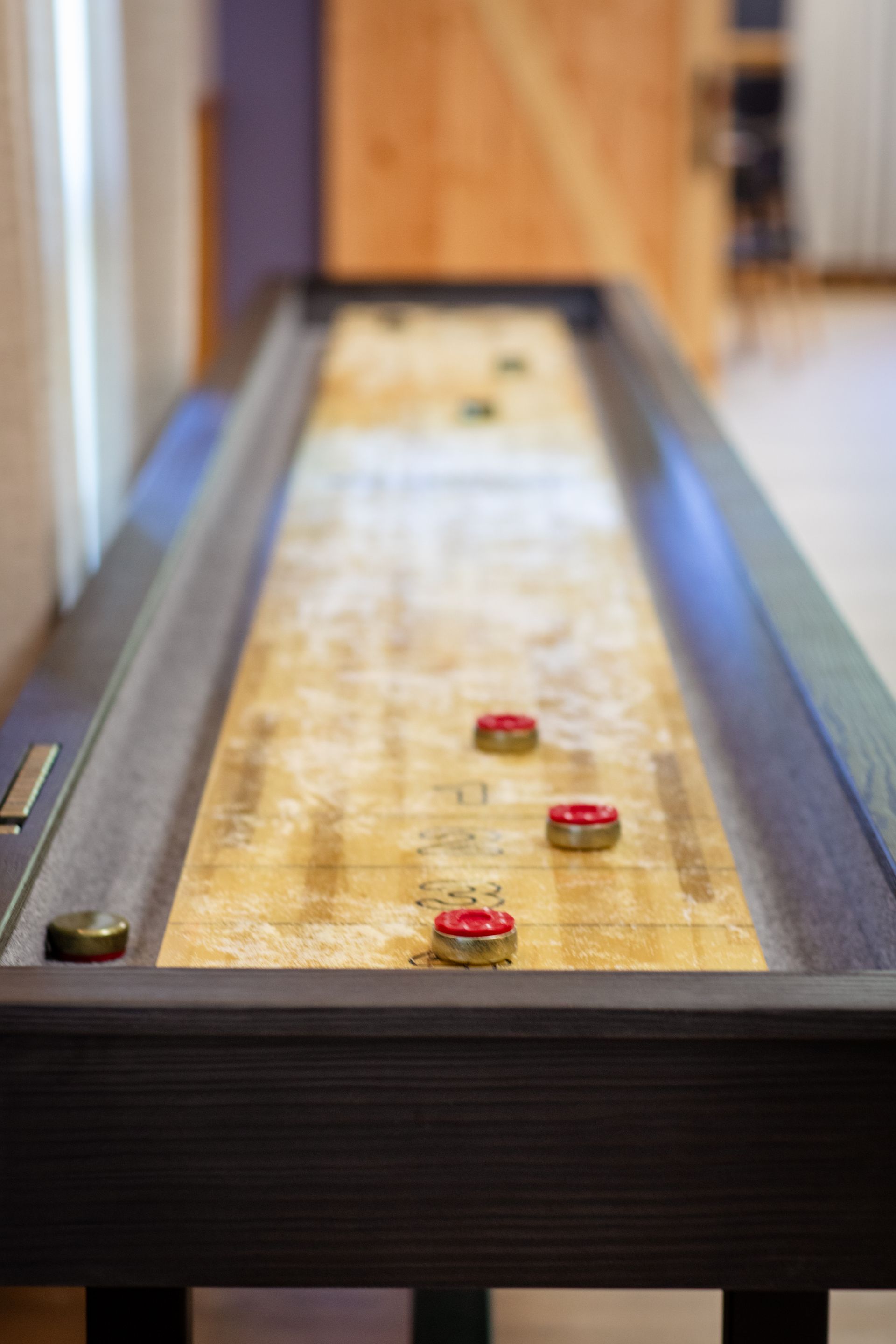 Shuffleboard table with several pucks on a long wooden lane indoors