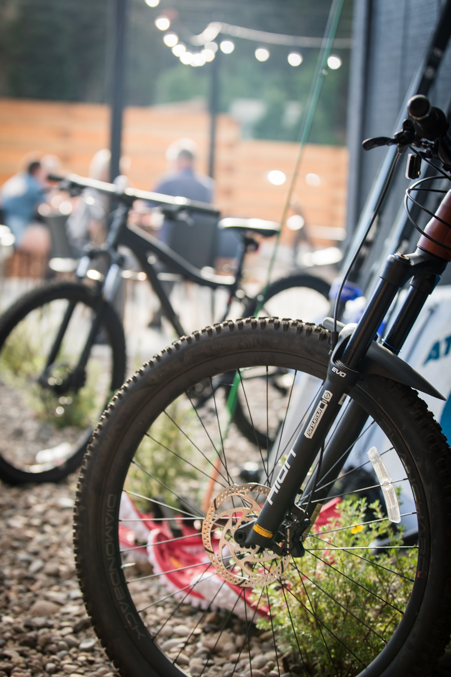 Bicycles parked outdoors near a brick building, with a close-up of a bike wheel and red flower pot in front.