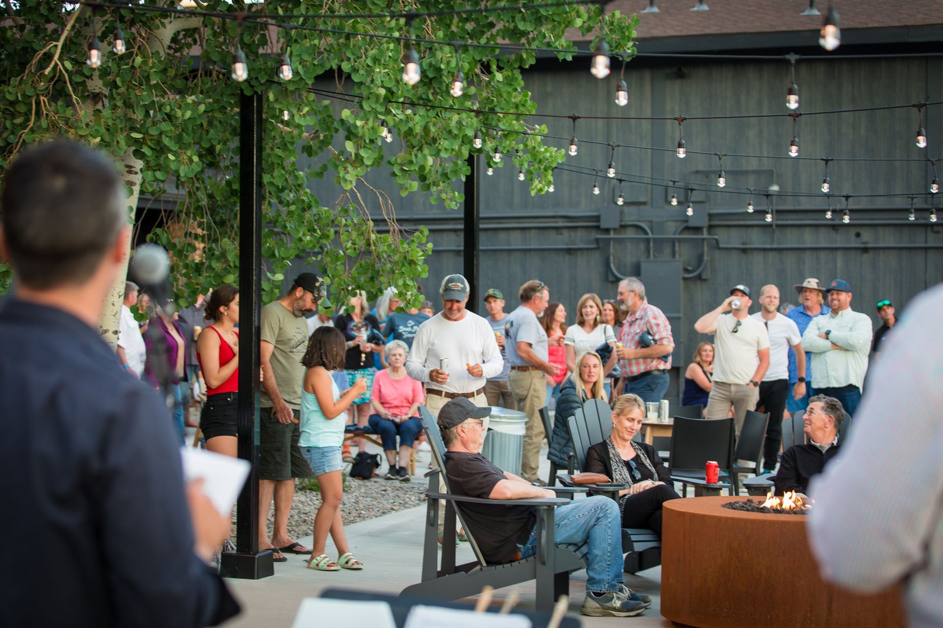 People gathered at an outdoor evening event with string lights and tables.