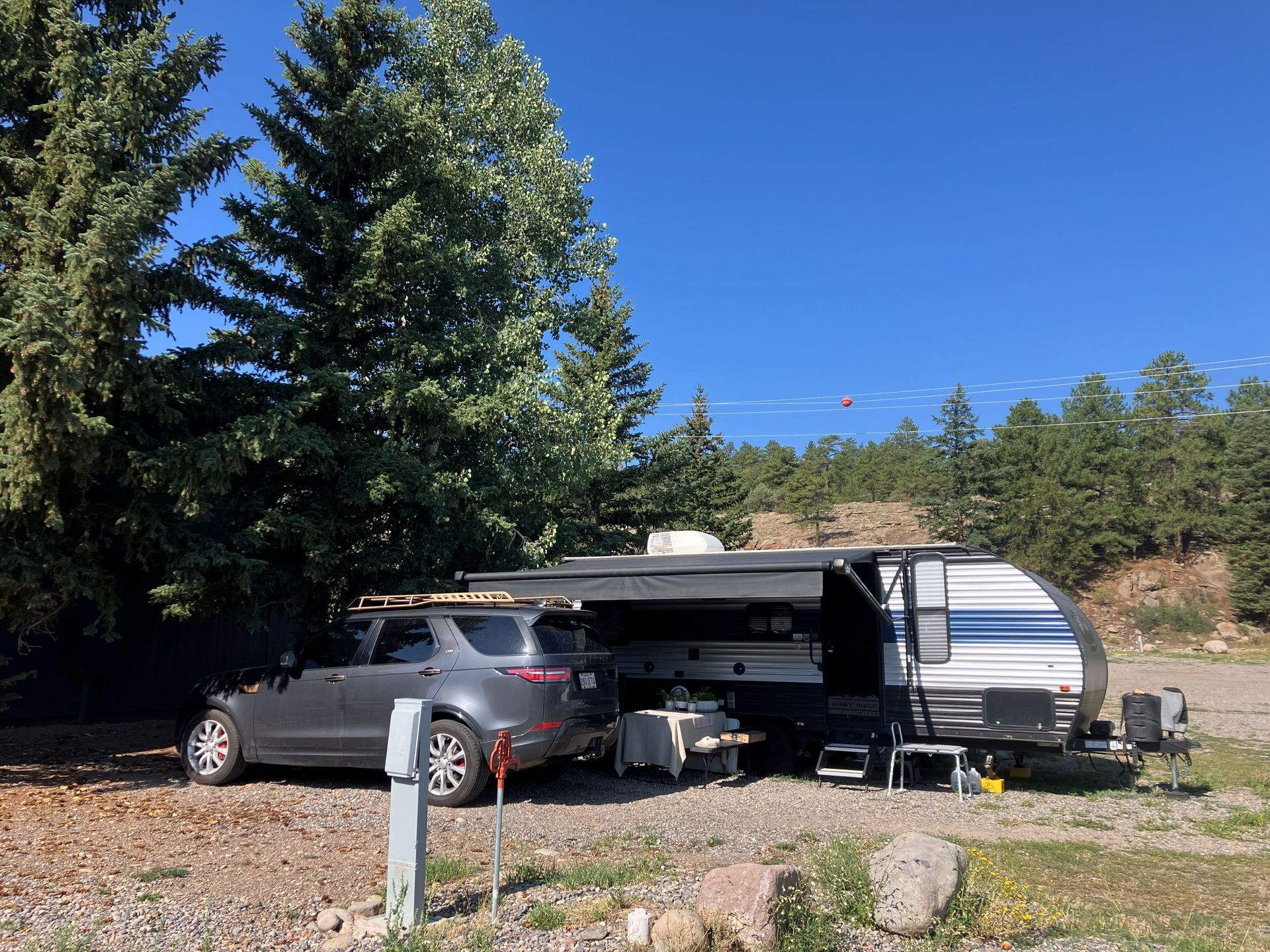 A gray SUV and an RV are parked in a gravel lot with number sign.