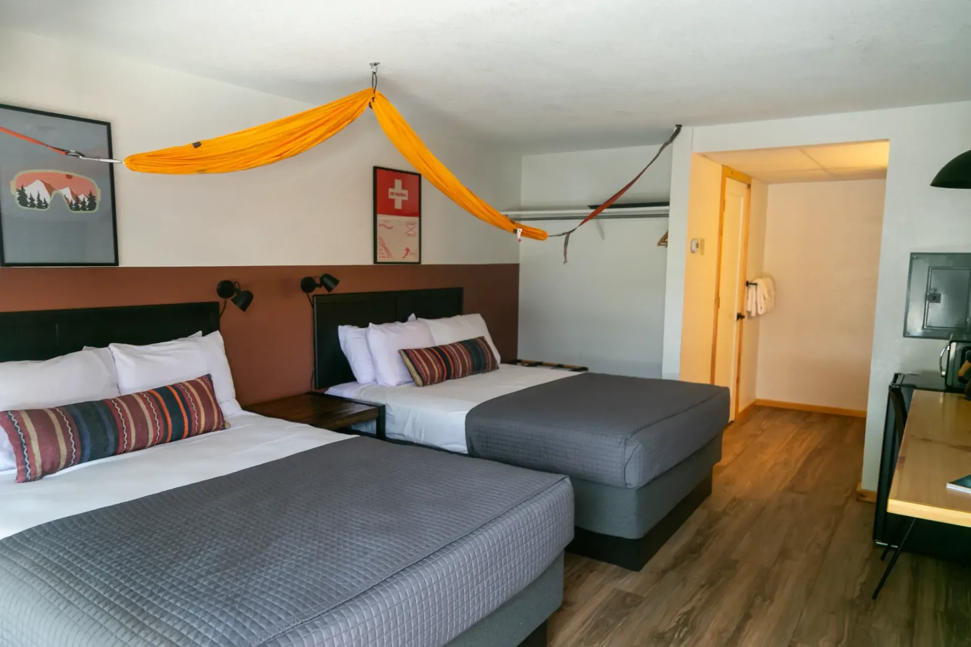 A hotel room with two queen beds, dark wood headboards, and a bright yellow hammock strung across the ceiling.