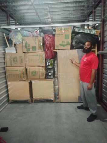 Man standing beside stacked cardboard boxes in a storage area with a metal ceiling
