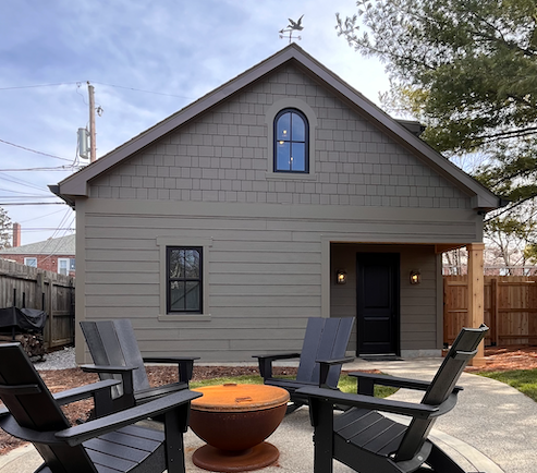 A entertainers dream backyard with a fire pit and chairs in front of it. Garage with office or guest room