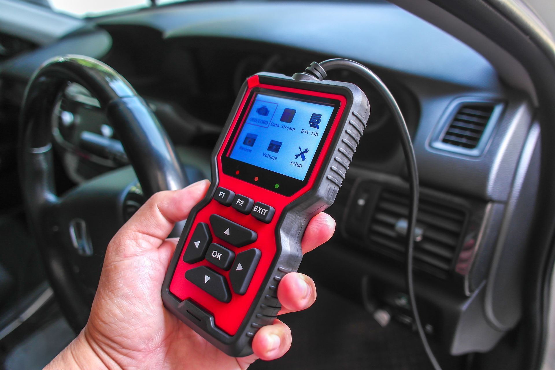Hand holding a red automotive diagnostic scanner inside a car interior | Dick Wolfe's Garage