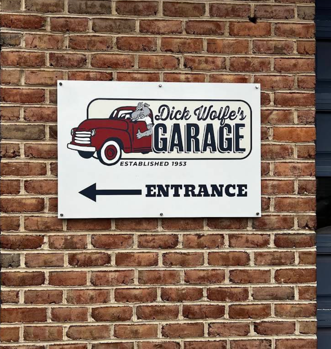 White sign on brick wall for shop with left-pointing arrow and “Entrance” text | Dick Wolfe's Garage