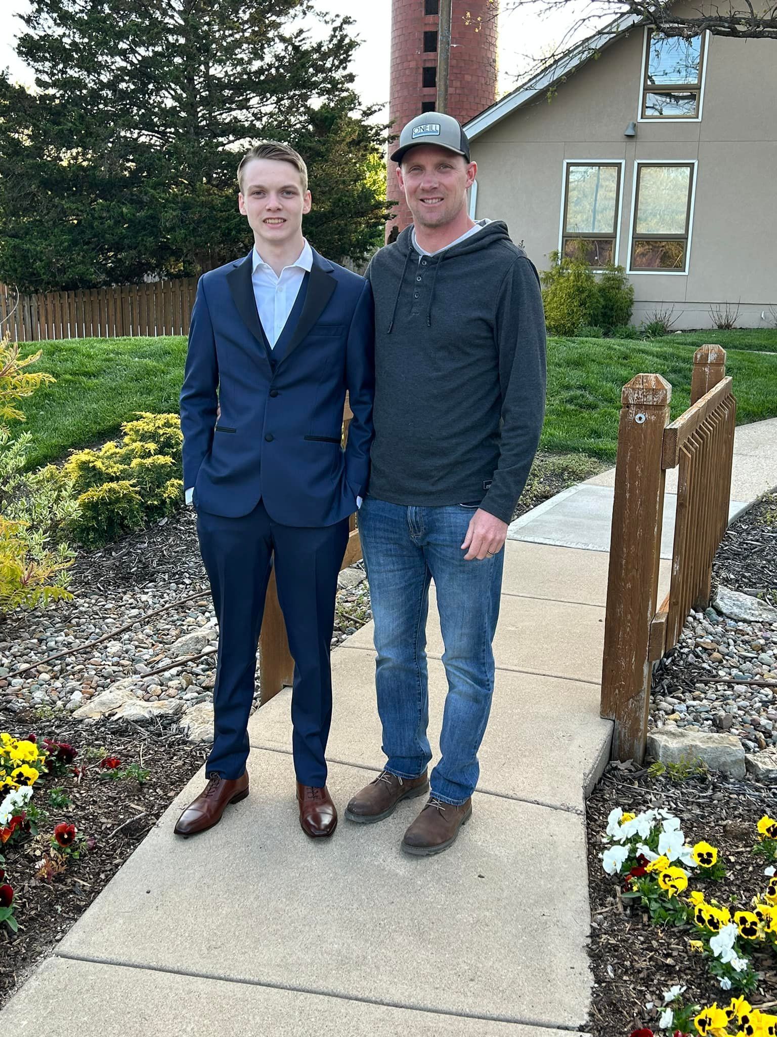 Two men standing next to each other on a sidewalk in front of a house